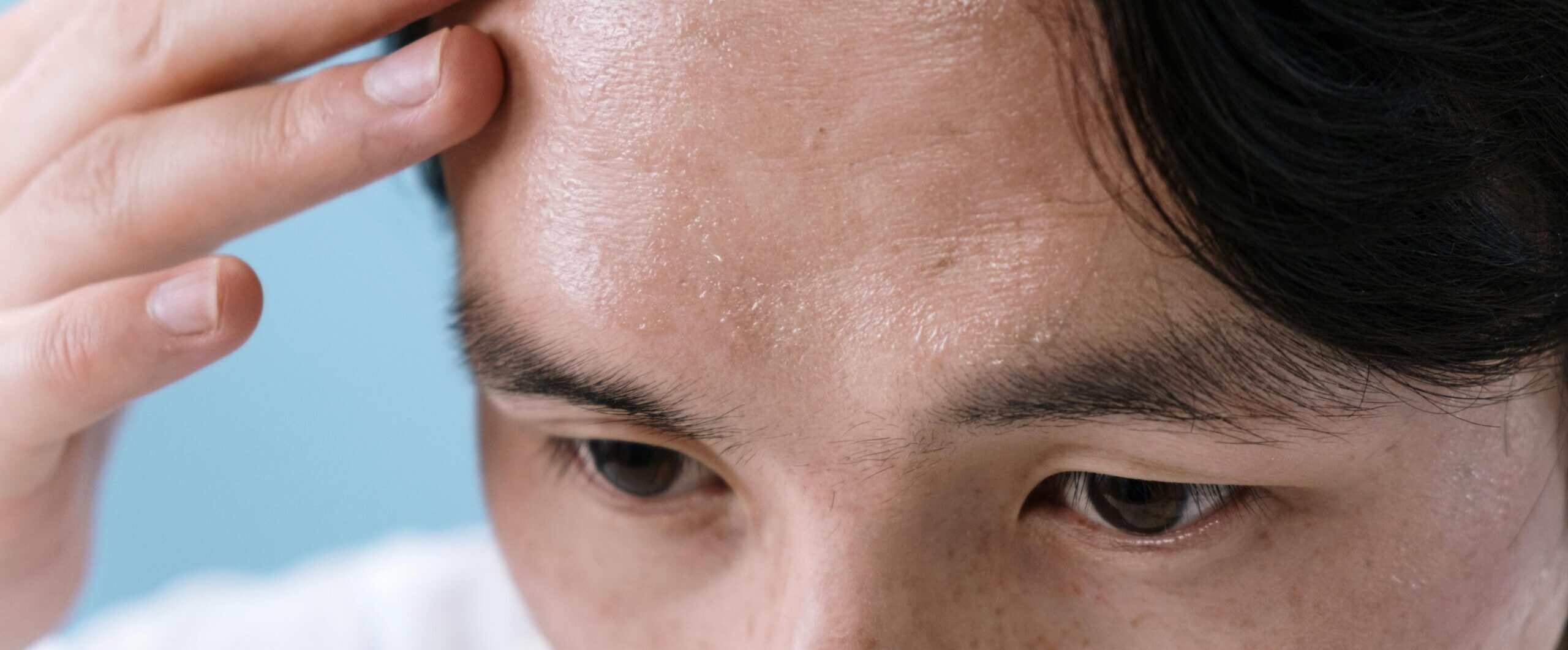 Close-up of a man with sweat on his forehead, touching it with his hand, conveying stress or illness.