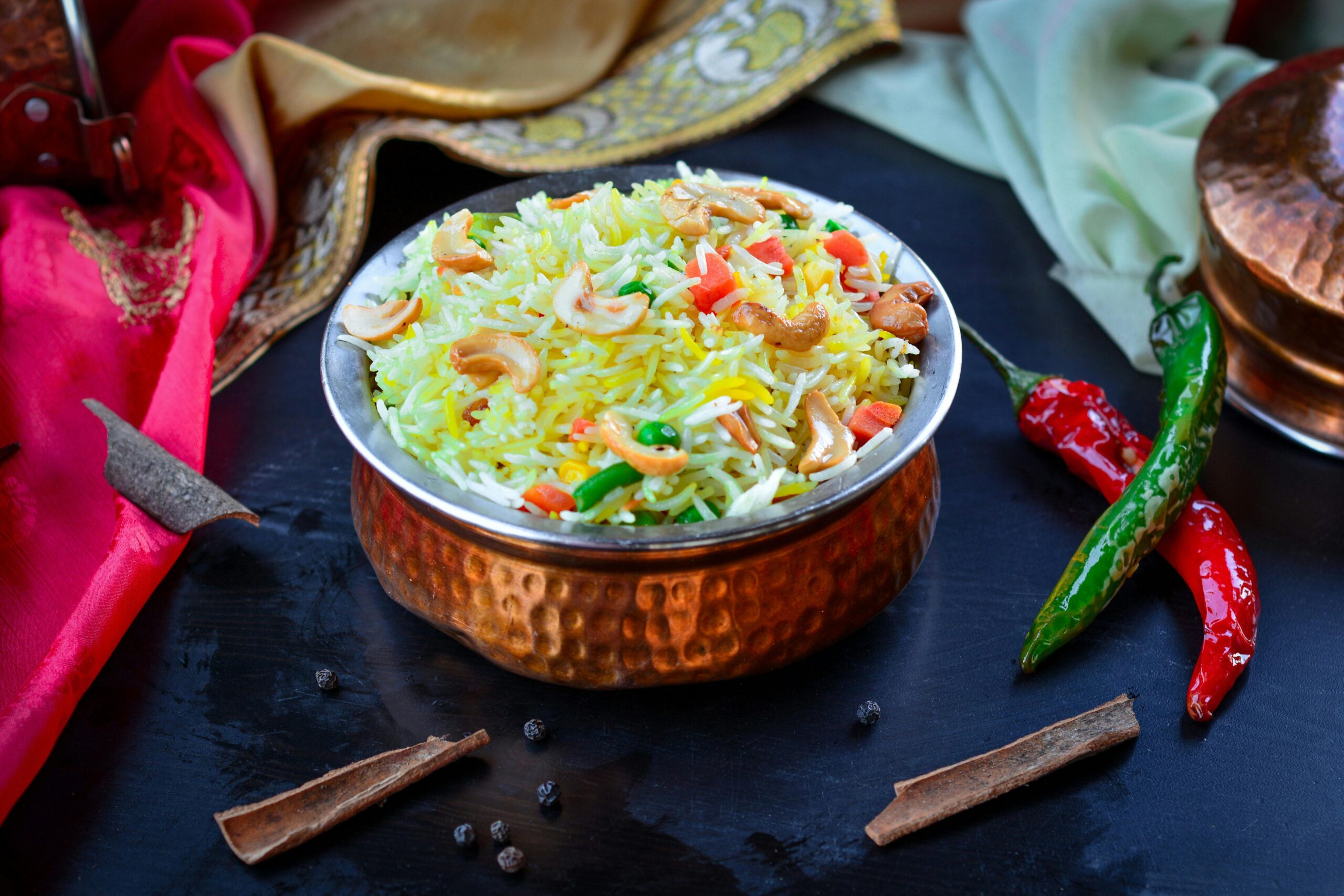 Bright Indian biryani with vegetables and nuts in a copper bowl, garnished with spices and chilies, best rice for biryani.
