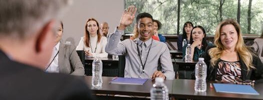 Businesspeople in a conference room engaging in a discussion, with a man raising his hand.